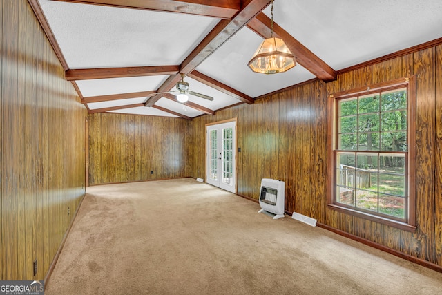 carpeted spare room with ceiling fan, french doors, vaulted ceiling with beams, heating unit, and a textured ceiling