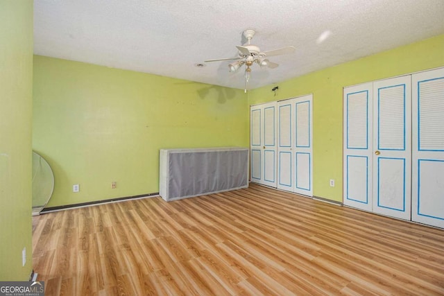 unfurnished bedroom featuring ceiling fan, light hardwood / wood-style flooring, a textured ceiling, and two closets