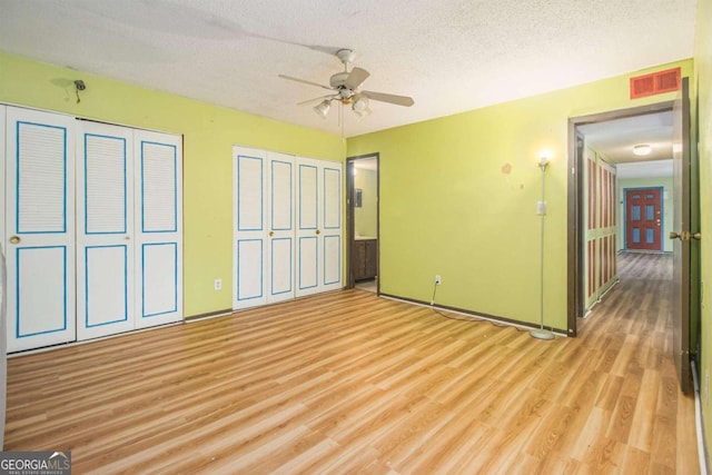 unfurnished bedroom with ceiling fan, two closets, a textured ceiling, and light hardwood / wood-style flooring