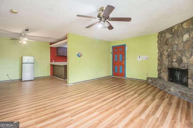 unfurnished living room with ceiling fan, a textured ceiling, hardwood / wood-style floors, and a stone fireplace