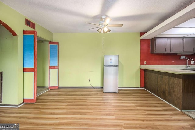 kitchen with a textured ceiling, sink, light hardwood / wood-style flooring, ceiling fan, and stainless steel fridge