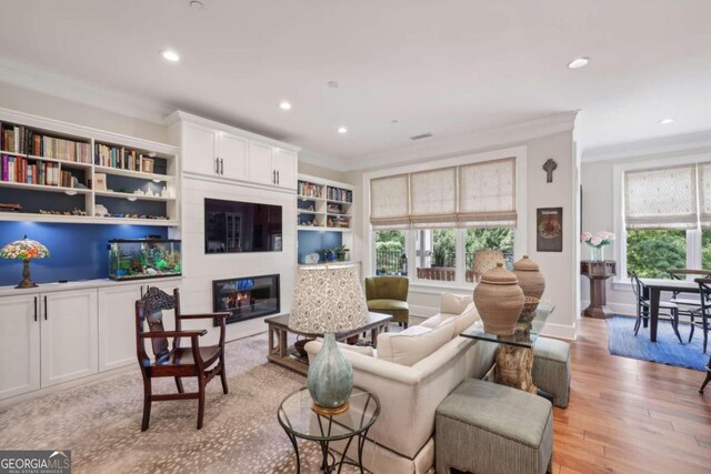 living room featuring built in shelves, light hardwood / wood-style flooring, a large fireplace, and ornamental molding