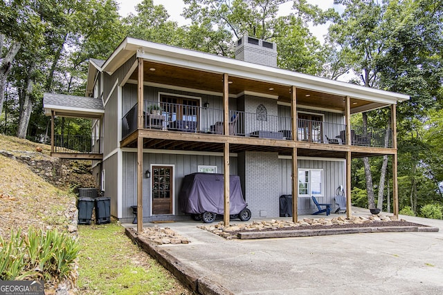 rear view of house featuring board and batten siding, brick siding, a chimney, and a balcony