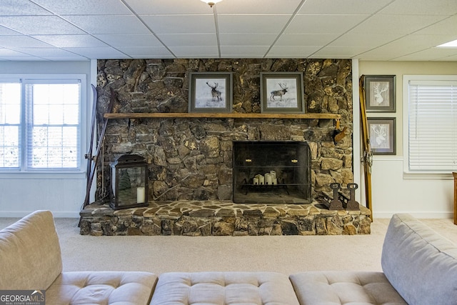 living area with carpet floors, a paneled ceiling, a stone fireplace, and baseboards