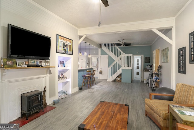 living room featuring a wood stove, crown molding, hardwood / wood-style flooring, ceiling fan, and a textured ceiling