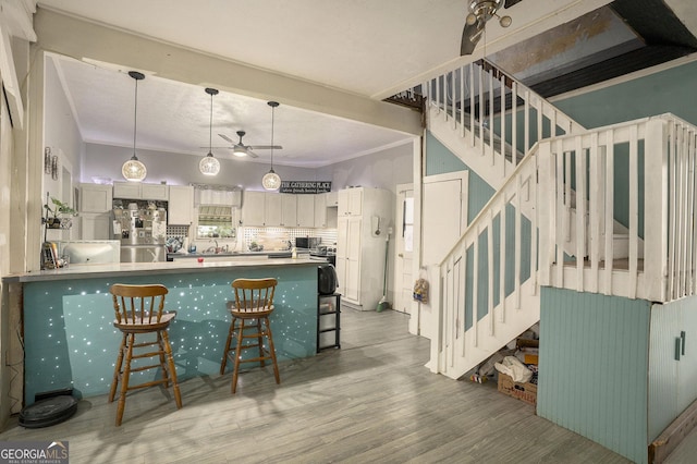 kitchen with light wood-type flooring, backsplash, a breakfast bar area, white cabinetry, and stainless steel refrigerator