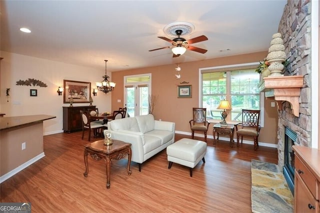 living room with light wood-type flooring, ceiling fan with notable chandelier, a stone fireplace, and french doors