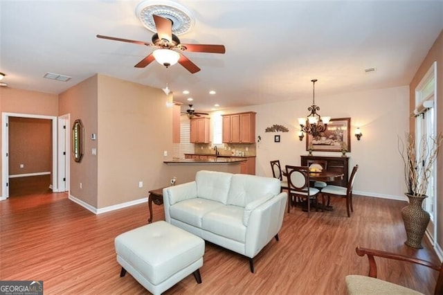 living room featuring ceiling fan with notable chandelier, light hardwood / wood-style flooring, and sink