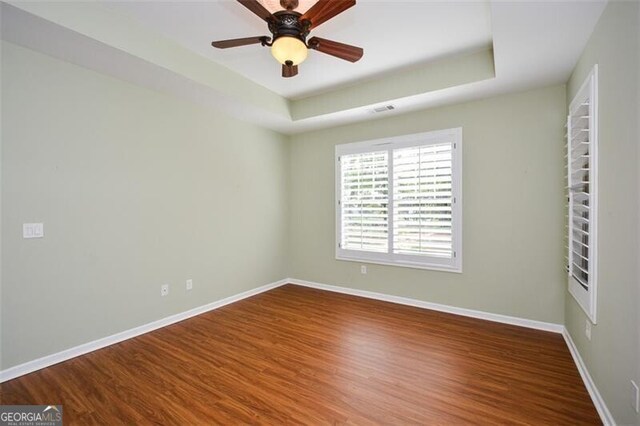 empty room with a raised ceiling, wood-type flooring, and ceiling fan