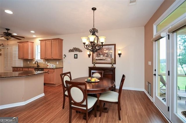 dining area featuring ceiling fan with notable chandelier, dark wood-type flooring, and sink