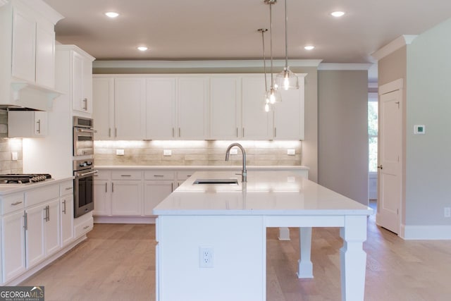 kitchen with a center island with sink, appliances with stainless steel finishes, sink, white cabinetry, and decorative light fixtures