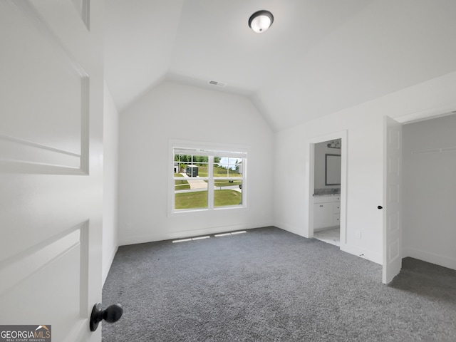 unfurnished bedroom with ensuite bath, vaulted ceiling, and carpet