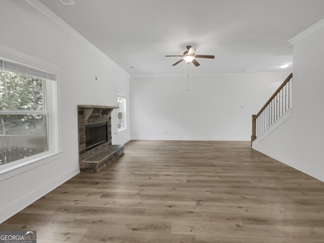 unfurnished living room featuring a stone fireplace, ceiling fan, ornamental molding, and hardwood / wood-style floors