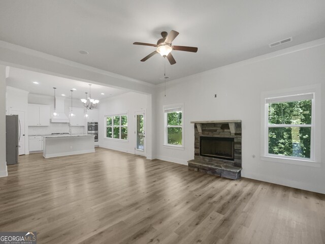 unfurnished living room featuring ceiling fan with notable chandelier, a fireplace, and light hardwood / wood-style floors