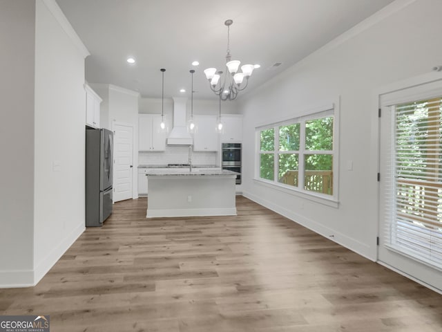 kitchen with backsplash, hanging light fixtures, light hardwood / wood-style flooring, stainless steel appliances, and a center island with sink