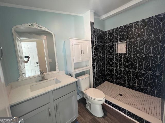 bathroom with ornamental molding, vanity, tiled shower, hardwood / wood-style flooring, and toilet