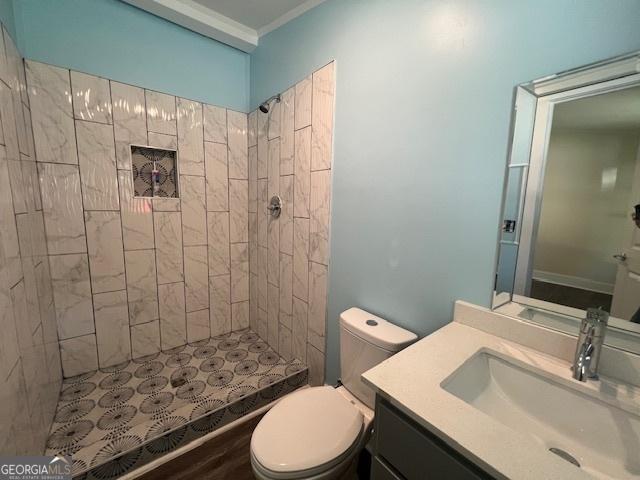 bathroom with crown molding, hardwood / wood-style floors, toilet, tiled shower, and vanity