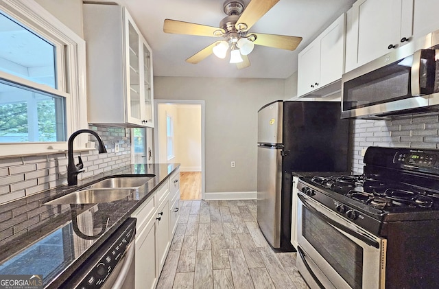 kitchen with sink, light wood-type flooring, appliances with stainless steel finishes, dark stone counters, and white cabinets