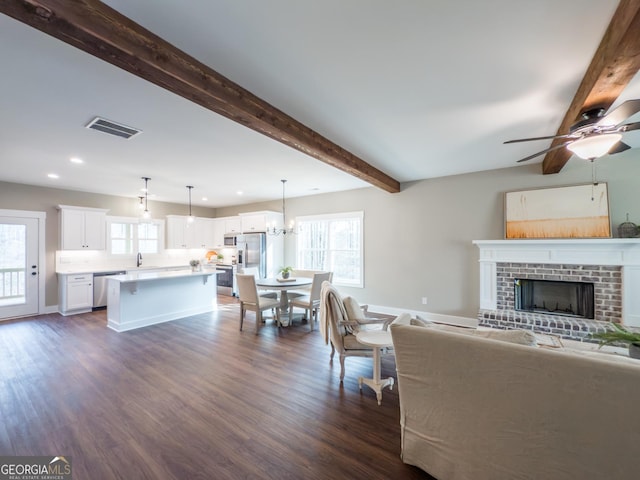 living room with dark hardwood / wood-style flooring, beam ceiling, a fireplace, and a healthy amount of sunlight