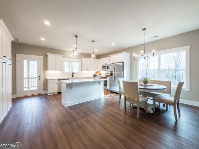 kitchen featuring dark wood-type flooring, white cabinetry, a center island, appliances with stainless steel finishes, and pendant lighting