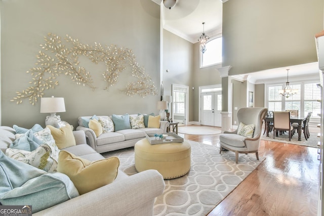 living room featuring a towering ceiling, decorative columns, crown molding, a notable chandelier, and light hardwood / wood-style floors