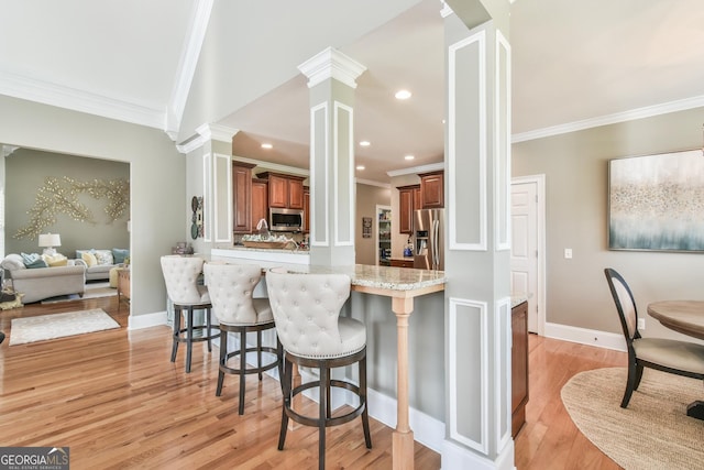 kitchen with kitchen peninsula, appliances with stainless steel finishes, light stone counters, ornamental molding, and a breakfast bar