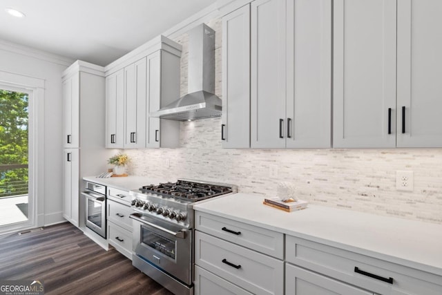 kitchen featuring wall chimney range hood, dark wood-type flooring, stainless steel appliances, backsplash, and white cabinetry