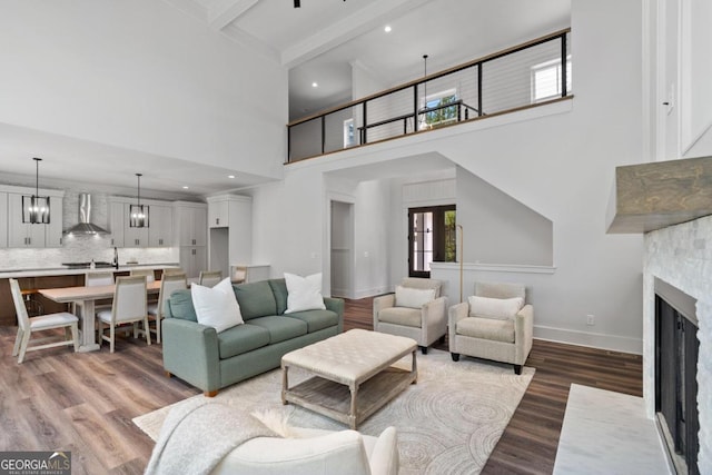 living room with a fireplace, beamed ceiling, wood-type flooring, and a high ceiling