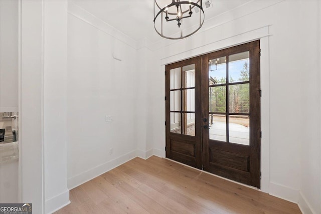 doorway to outside with an inviting chandelier, ornamental molding, french doors, and light wood-type flooring