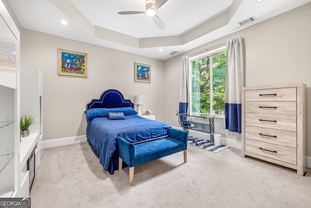 bedroom featuring a tray ceiling, light colored carpet, and ceiling fan