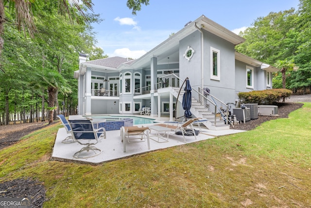 back of property with a patio, a balcony, cooling unit, a swimming pool with hot tub, and a yard