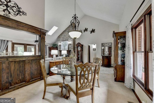 dining room featuring ceiling fan, light colored carpet, high vaulted ceiling, and a skylight