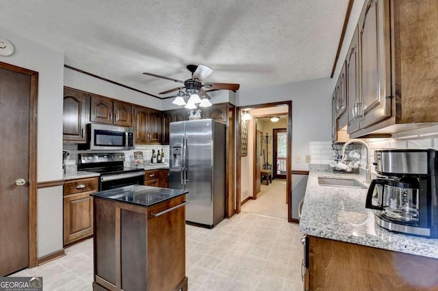 kitchen featuring sink, a center island, stainless steel appliances, tasteful backsplash, and light stone counters