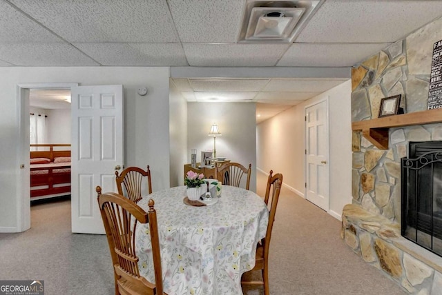 carpeted dining area with a paneled ceiling and a stone fireplace