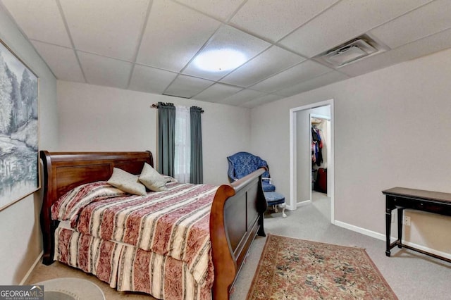 carpeted bedroom featuring a drop ceiling and a walk in closet