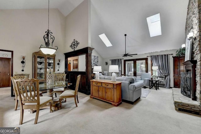 carpeted living room featuring ceiling fan, a fireplace, high vaulted ceiling, and a skylight