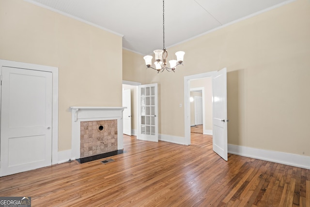 unfurnished living room featuring a tile fireplace, crown molding, wood-type flooring, and an inviting chandelier