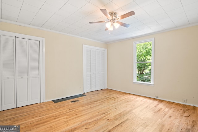 unfurnished bedroom with crown molding, light hardwood / wood-style floors, and multiple closets