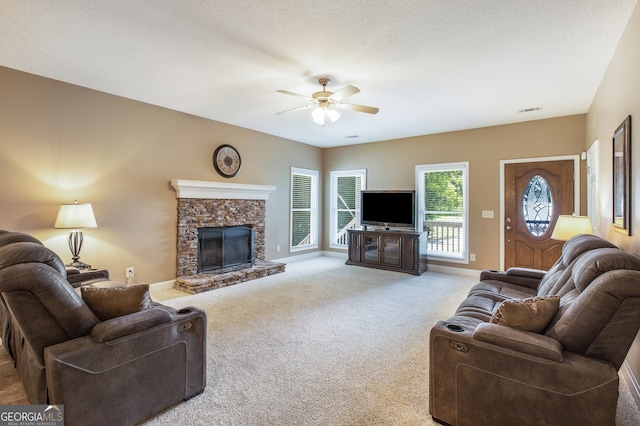 living room with a stone fireplace, a textured ceiling, carpet flooring, and ceiling fan