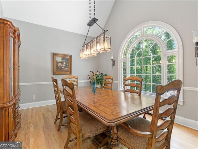 dining space with vaulted ceiling, an inviting chandelier, and light hardwood / wood-style flooring