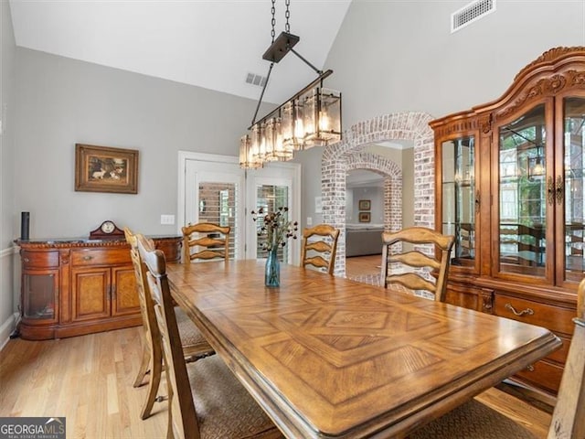 dining area featuring high vaulted ceiling, french doors, light hardwood / wood-style floors, and brick wall