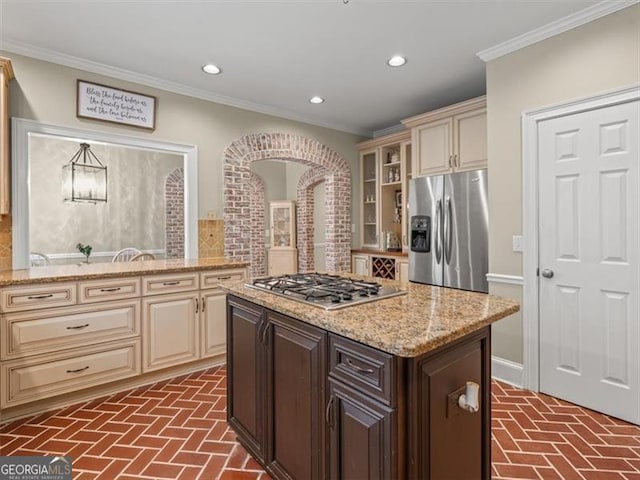 kitchen featuring appliances with stainless steel finishes, dark brown cabinets, light stone countertops, cream cabinets, and crown molding