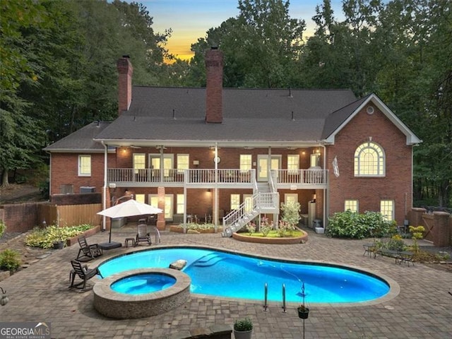 back house at dusk with a balcony, a patio area, and a swimming pool with hot tub