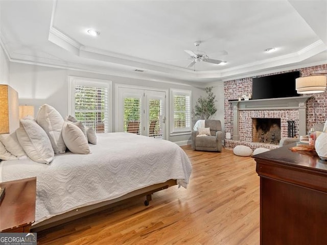 bedroom featuring ceiling fan, light wood-type flooring, a raised ceiling, and a brick fireplace