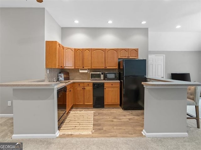 kitchen with kitchen peninsula, tasteful backsplash, black appliances, light wood-type flooring, and a breakfast bar area