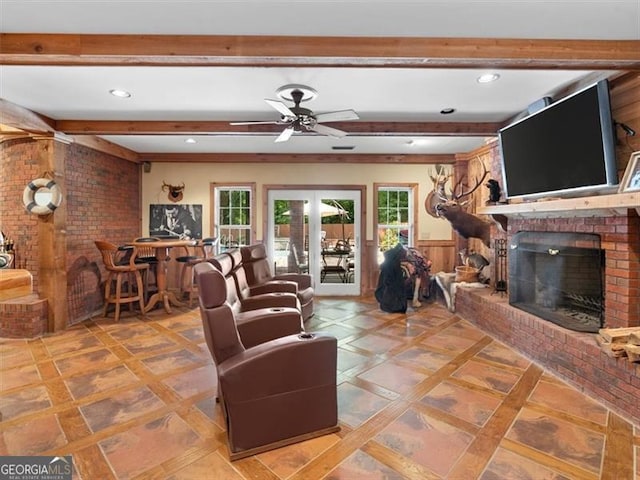 living room with ceiling fan, beam ceiling, brick wall, and a brick fireplace