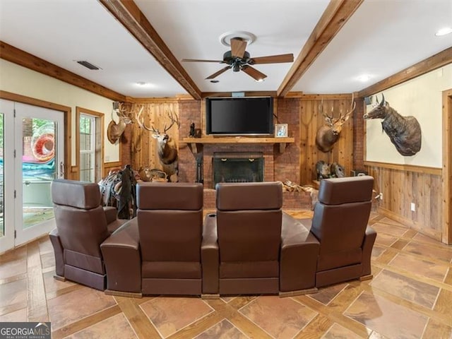 cinema featuring ceiling fan, wood walls, a brick fireplace, tile patterned floors, and beamed ceiling