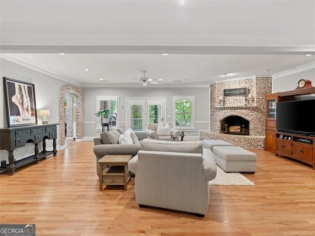 living room featuring ornamental molding, brick wall, light wood-type flooring, a fireplace, and ceiling fan