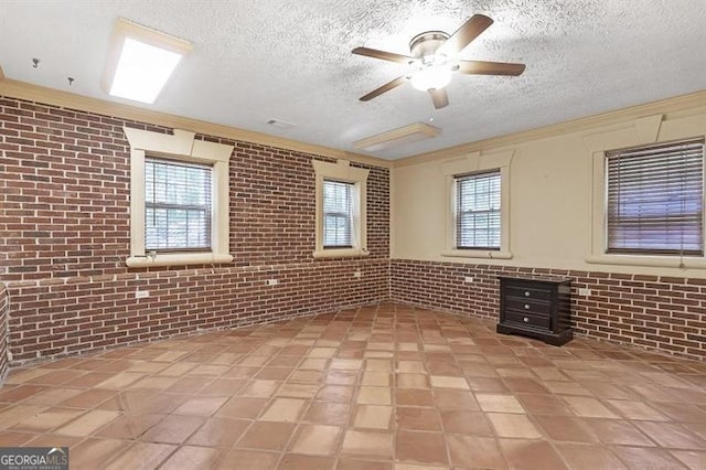 tiled empty room featuring ceiling fan, a textured ceiling, crown molding, and brick wall