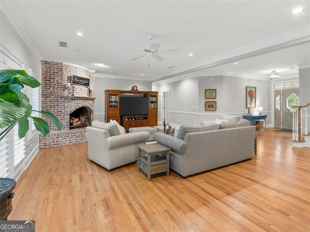 living room featuring light wood-type flooring, ornamental molding, ceiling fan, and a brick fireplace